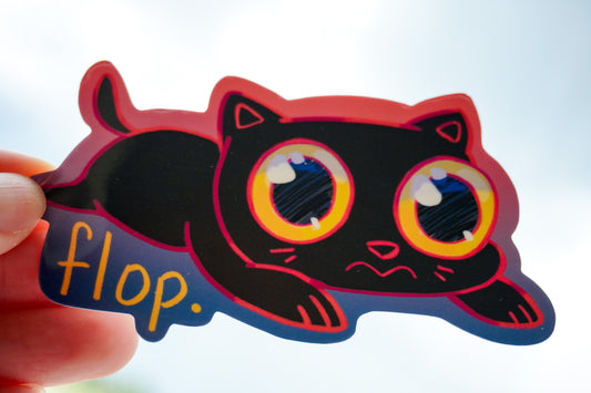 Black cat with red accents and 'flop.' text held by a hand against a light background