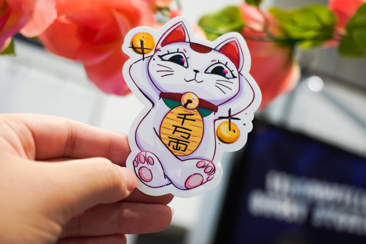 Hand holding a cartoon-style cat sticker with a blurred background