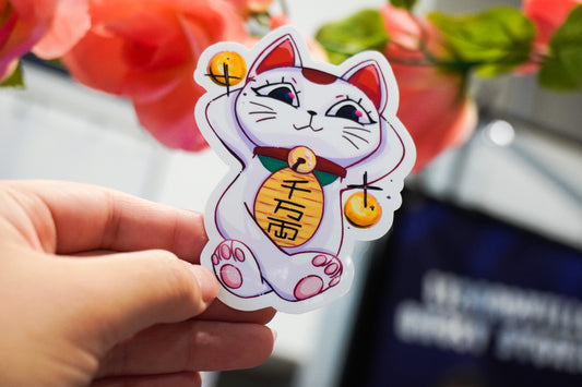 Hand holding a cartoon-style cat sticker with a blurred background