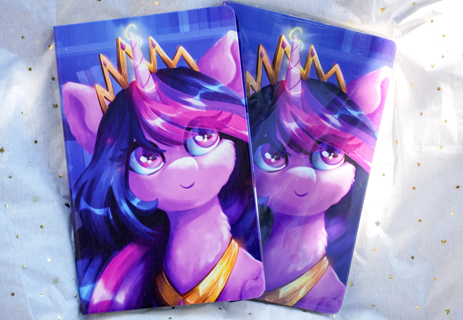 Two cartoon-style notebooks with a purple character wearing a crown on a light background